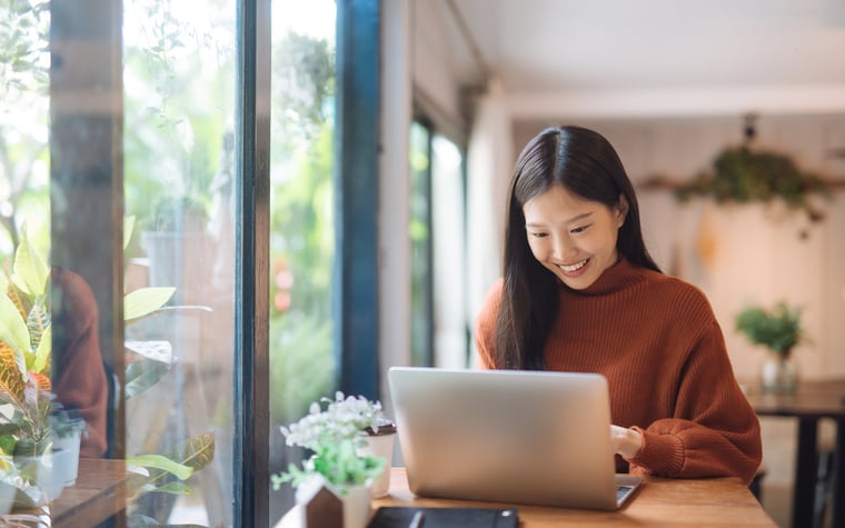 A young woman working on a laptop in a sunny cafe.
