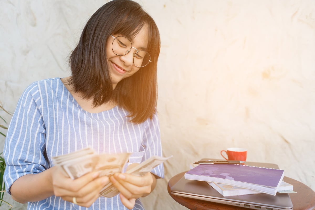 Young woman smiling as she counts cash in her hands.