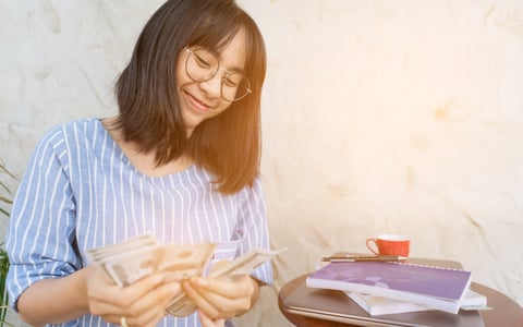 Young woman smiling as she counts cash in her hands.