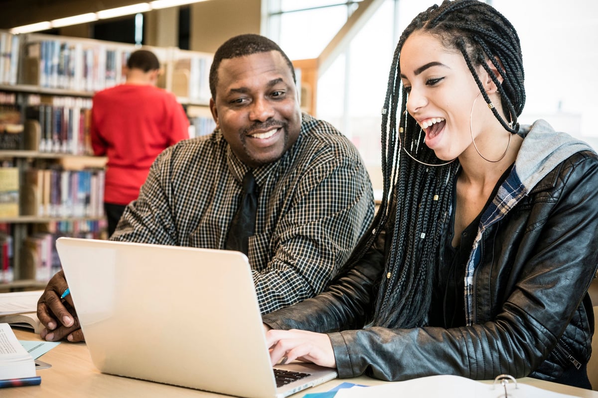 Young woman smiling using laptop next to adult male in a library.