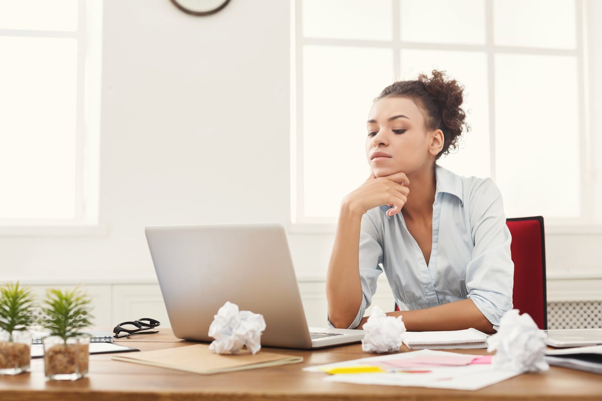 A woman looking at her laptop with papers on her desk.