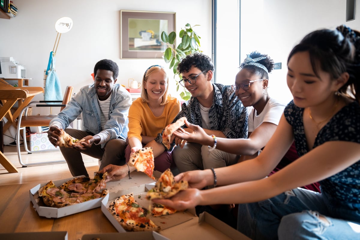 A group of friends eating pizza while sitting on the couch in an apartment.
