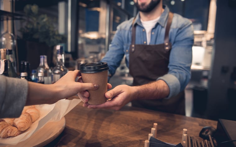 Un barista tendant une tasse de café à emporter à un client dans un coffeeshop.