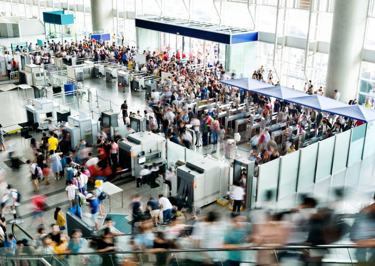 A busy airport security entrance with lots of people rushing through.