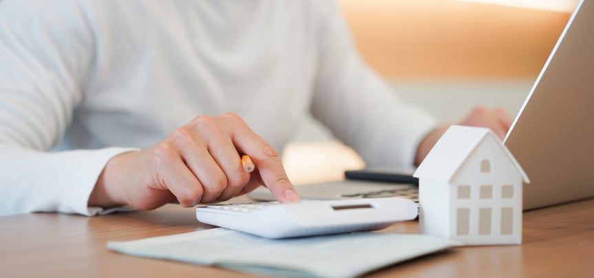 A hand on a calculator, and a small house