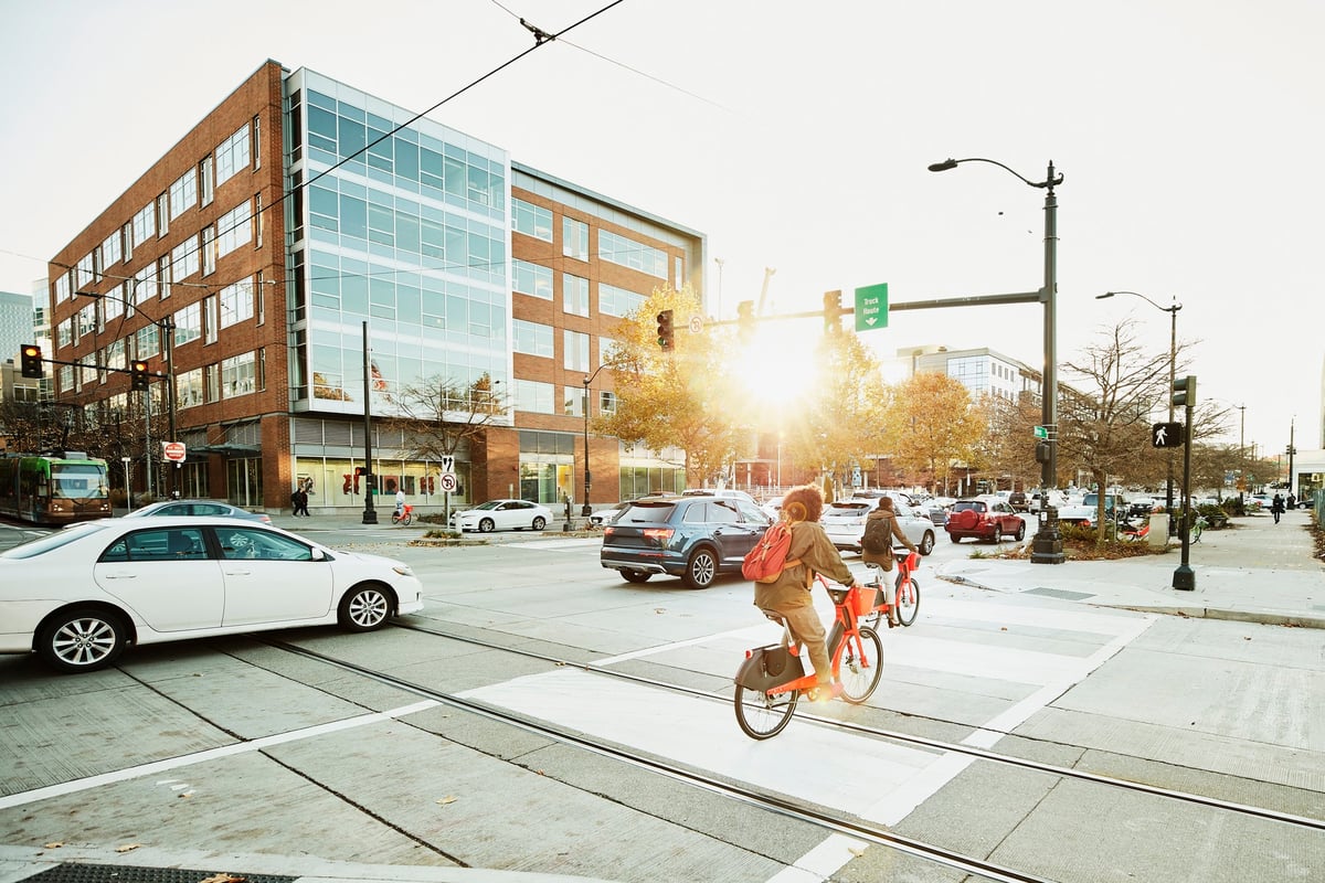 Cars driving through stoplights on a busy street as bikes ride by.