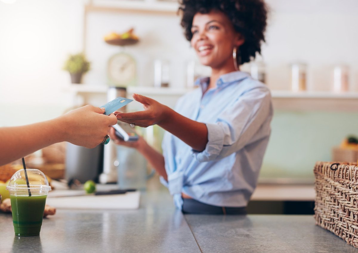 A customer handing their credit card over the counter to the cashier at a cafe.