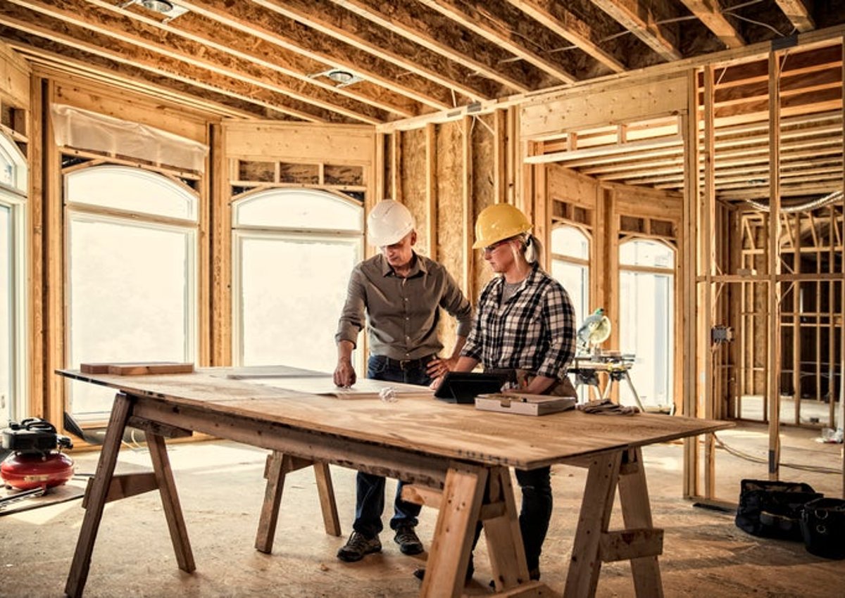 คนงานก่อสร้างสองคนกำลังดูพิมพ์เขียวบนโต๊ะในบ้านที่กำลังสร้าง