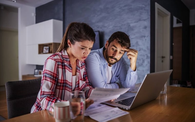 A couple looking worried about money, with a laptop and bills.