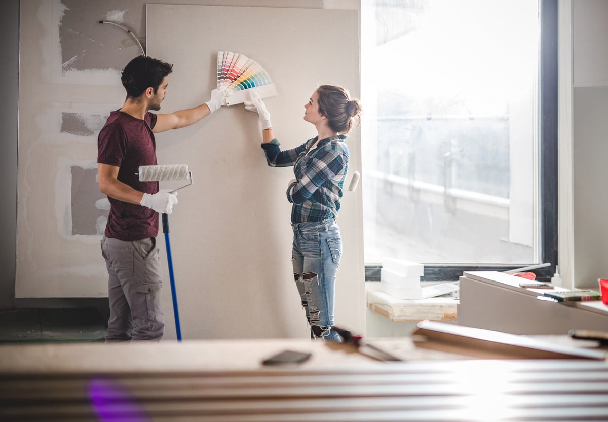 A young couple standing in their home renovation and picking out paint colors.