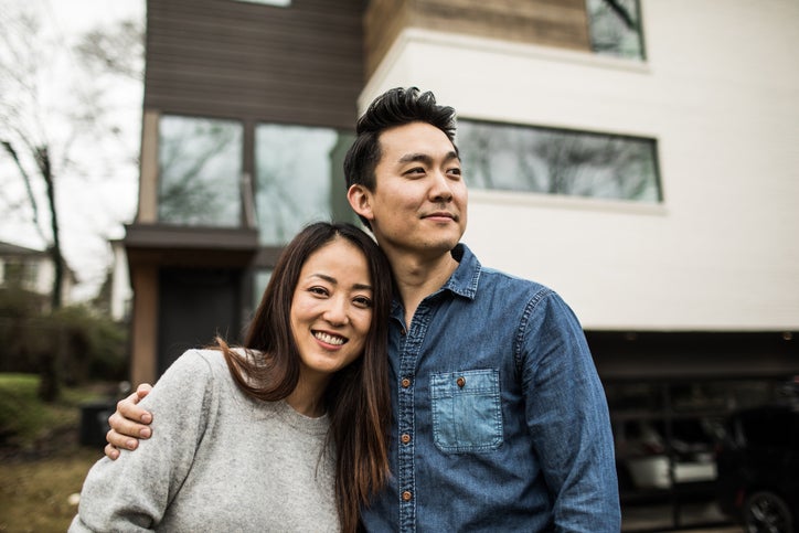 A young man and woman smiling while standing in front of their house.