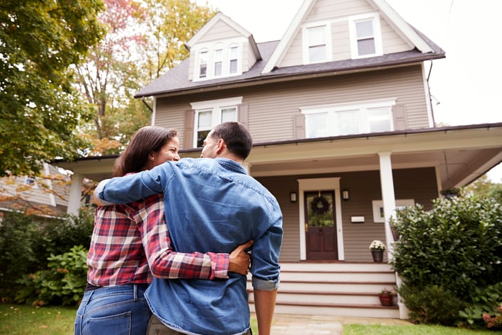 A couple with their arms around each other standing in front of their new house.