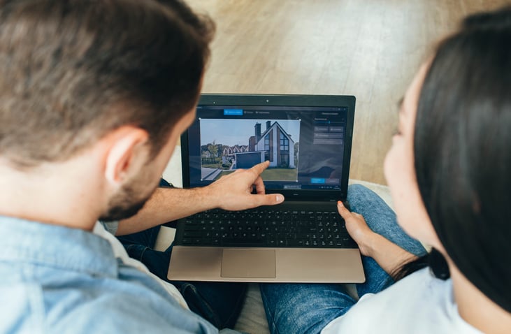 A man and woman sitting next to each other and looking at a house listing on their laptop.