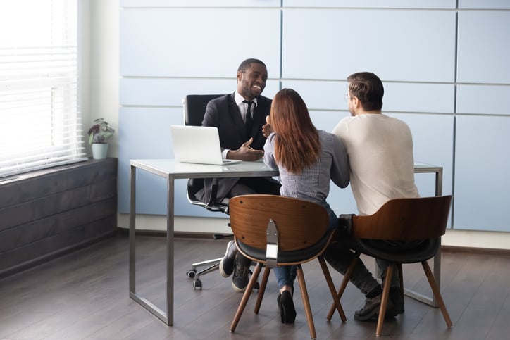 A man and woman sitting at a desk across from a bank representative and having a friendly discussion.