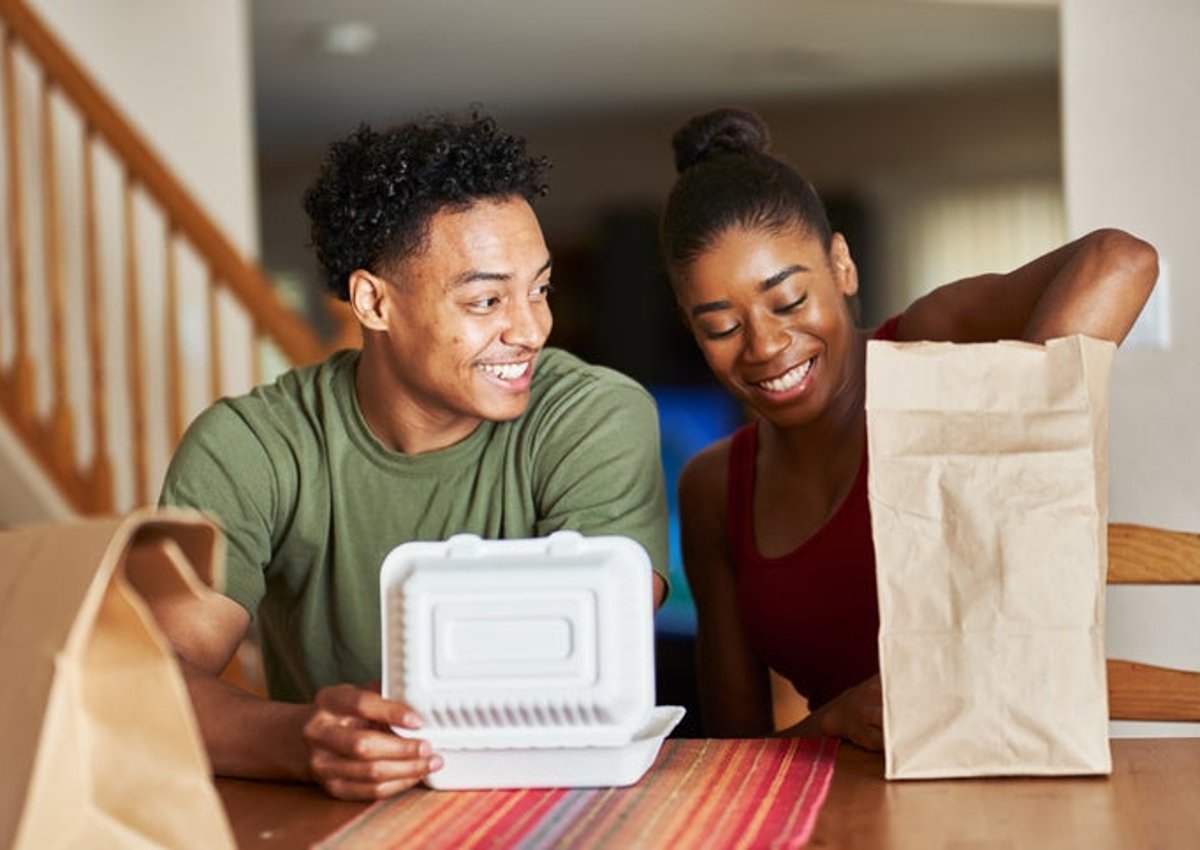 A man and woman sitting at their dining table and opening takeout food containers.