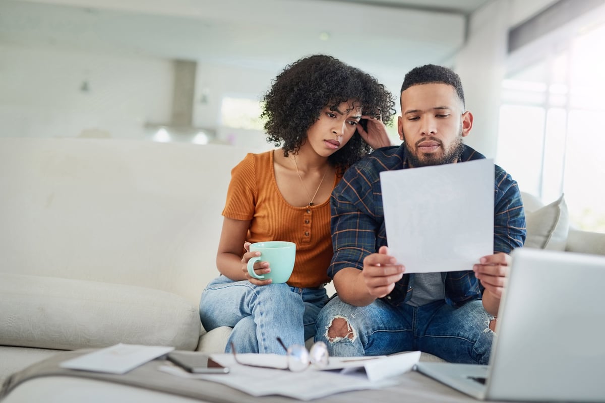 A couple looking distraught while reading bills on their couch.