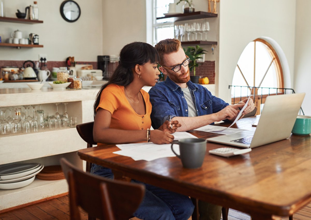 A couple reviewing bills together on a laptop while sitting in their kitchen.