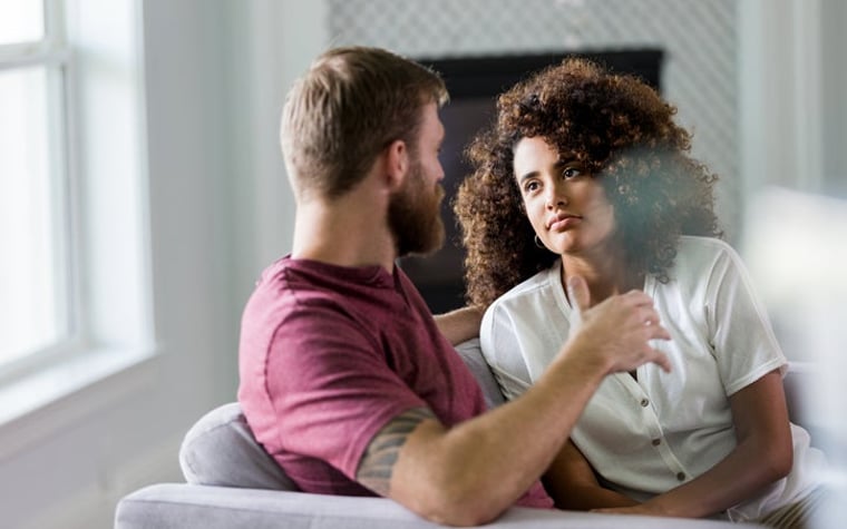 A man and a woman are sitting on a couch and having a serious conversation.