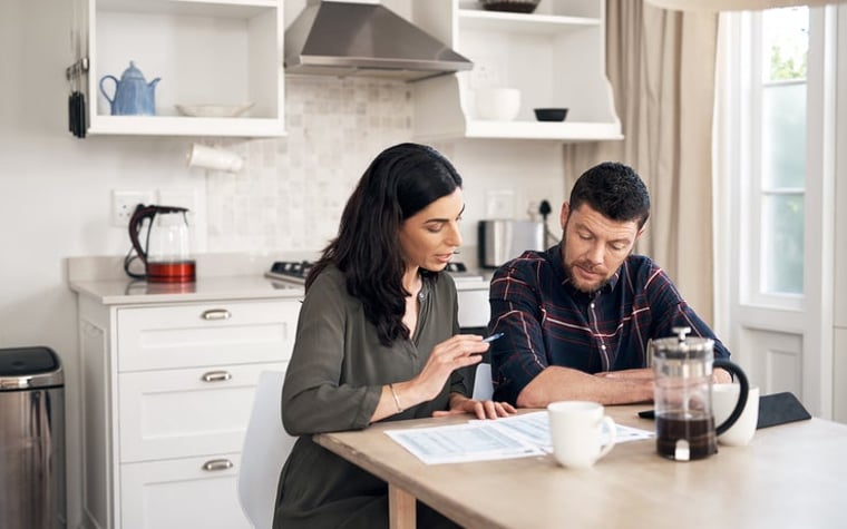 A man and a woman are sitting in their kitchen, talking, looking through papers.