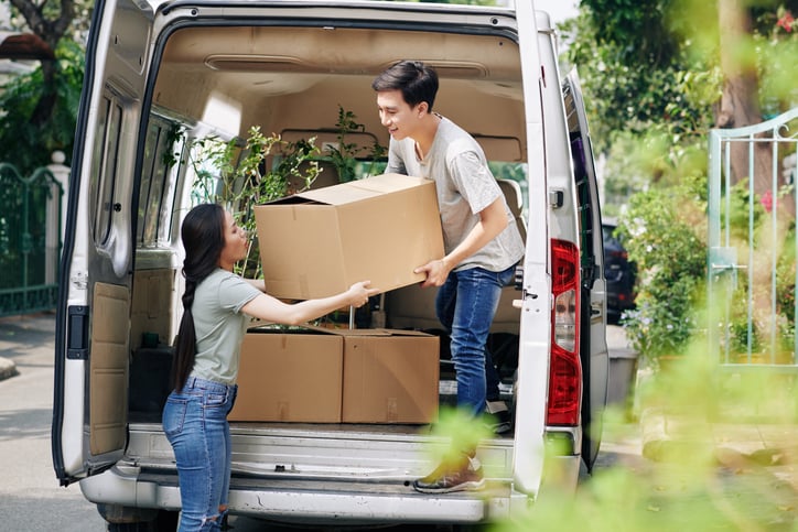 A man and woman unloading boxes from the back of a moving van.