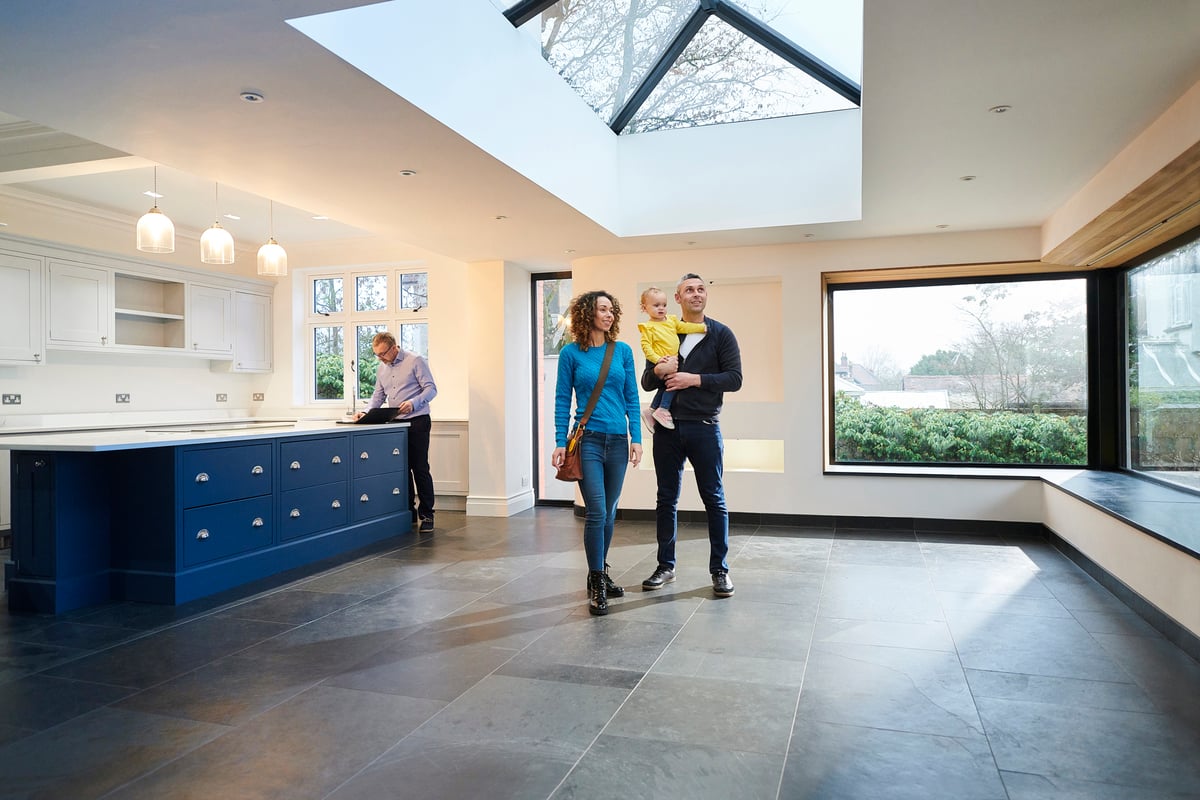 A couple holding their baby while walking through an empty eat-in kitchen with their realtor.
