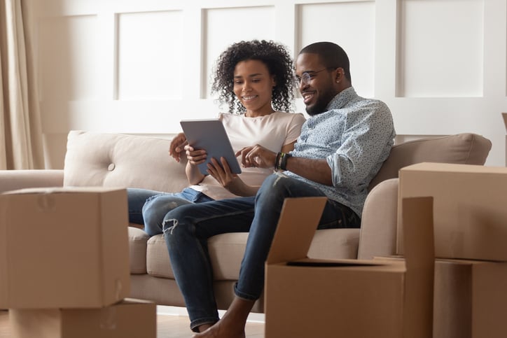 A couple looks at a pad while sitting on a couch near moving boxes
