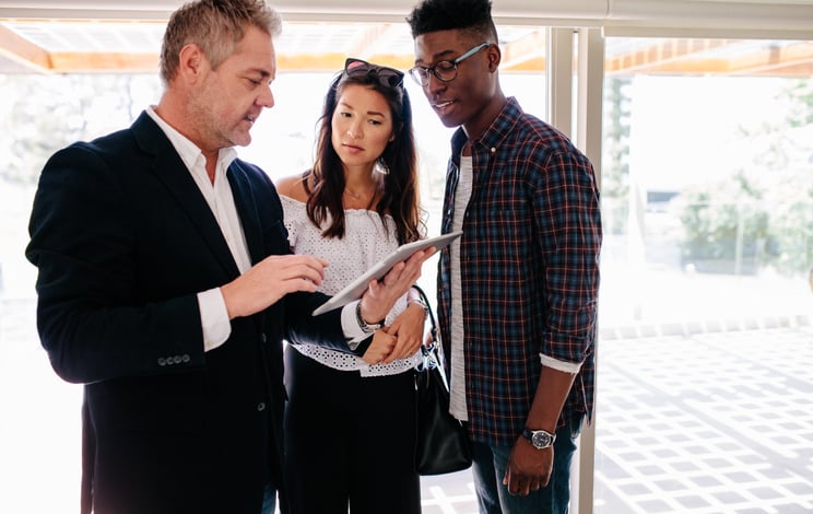 A young man and woman speaking with their realtor who's holding a tablet in an open house.