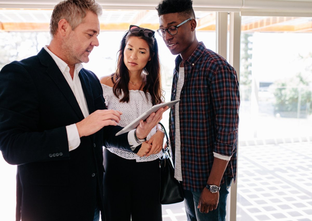 A young man and woman speaking with their realtor who's holding a tablet in an open house.