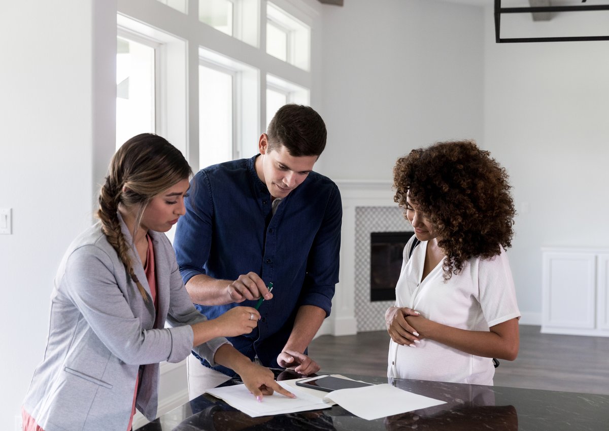 A couple standing in a new home with their realtor and signing papers.