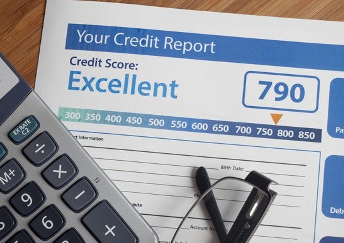 A credit report with an excellent score lying next to a calculator and a pair or reading glasses. 