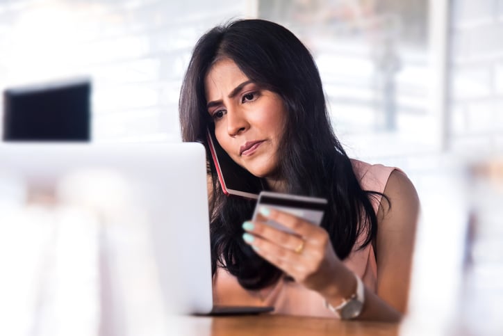A concerned woman at a laptop holding a credit card