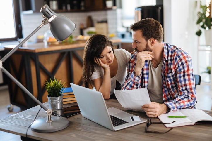 A worried couple looks at bills, with a laptop and a credit card on the table.