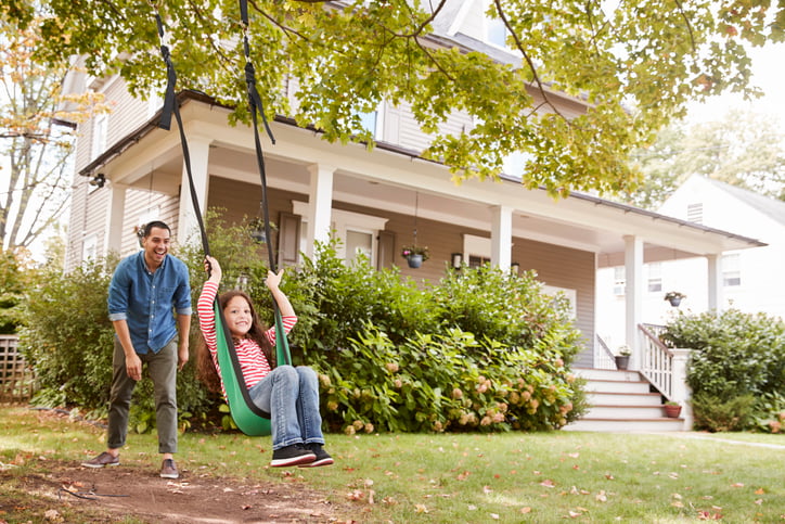 A smiling father pushing his laughing daughter on a tree swing in their front yard.