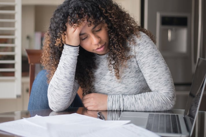 A woman looking worried, at a table with papers and a laptop.