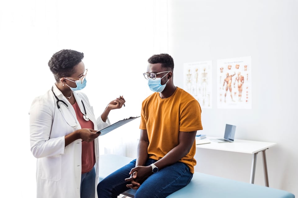 A patient sitting at the table in an exam room and speaking with the doctor.
