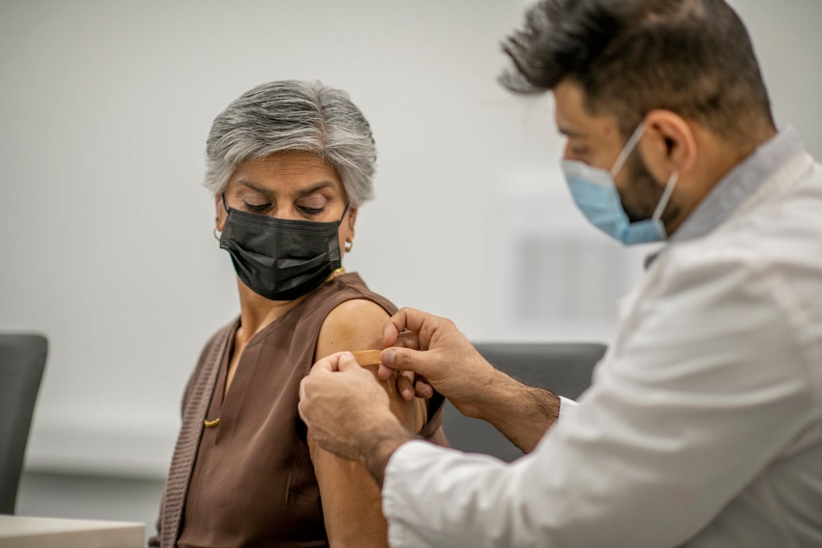 A doctor putting a band-aid on a person's arm after administering a vaccine shot.