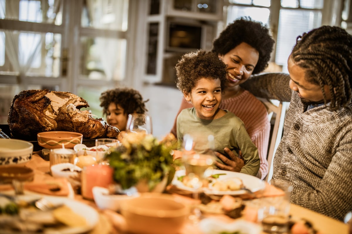 A smiling family seated around a Thanksgiving table full of food.