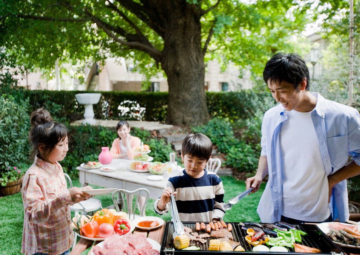 Two parents and two kids enjoying a backyard barbecue surrounded by green trees.