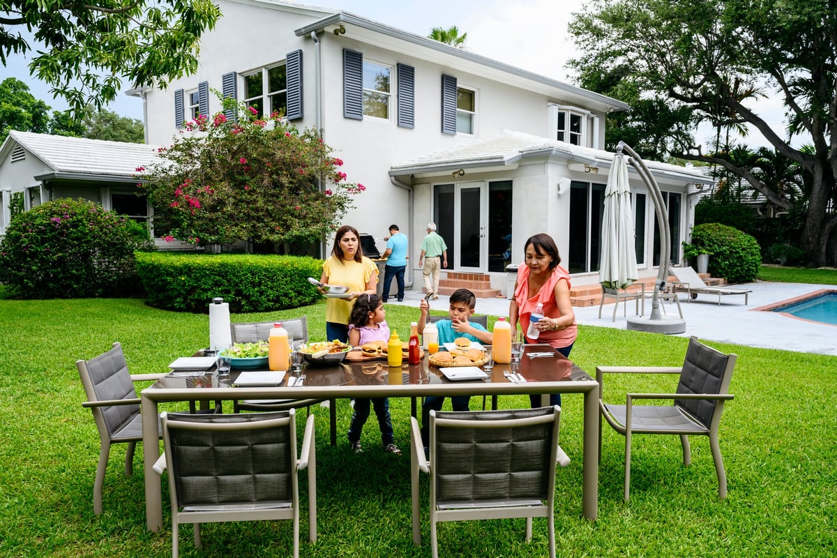 A family having lunch at a table on the lawn in their sunny backyard.