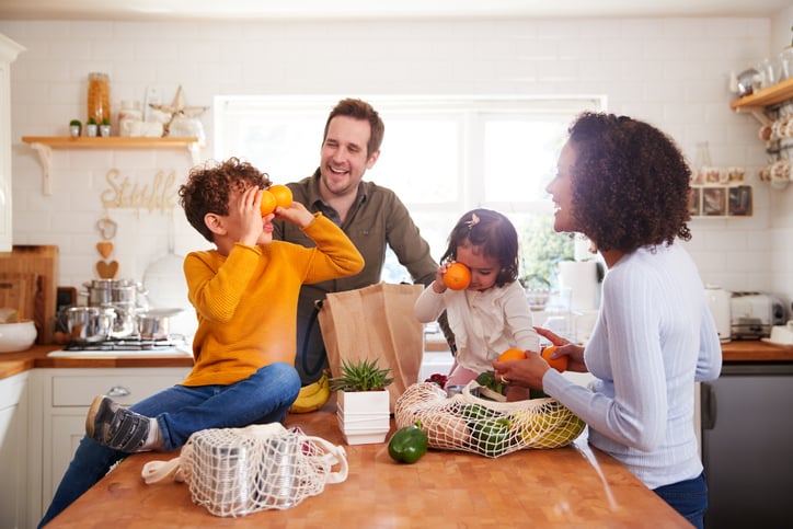 A mom, dad, son, and daughter unpacking bags of groceries in their kitchen and playing with the food.