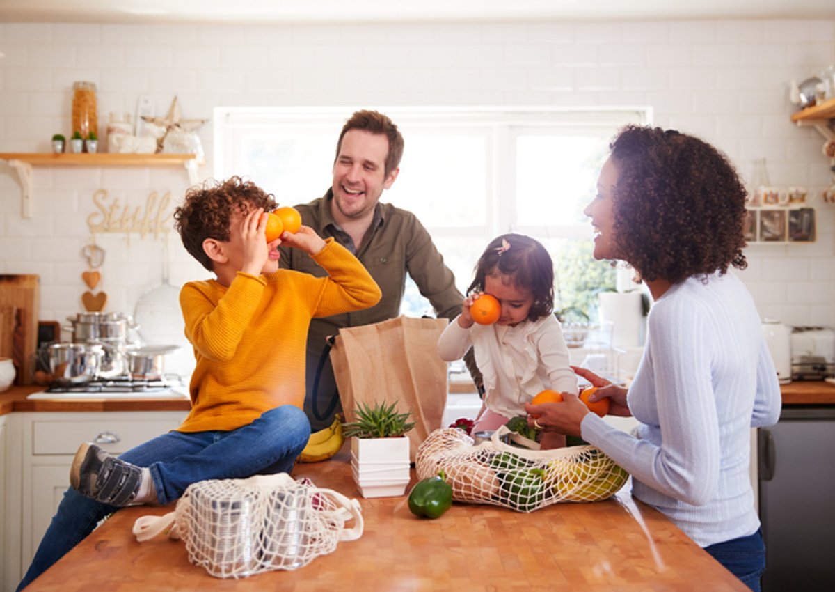 Une mère, un père, un fils et une fille déballant des sacs d'épicerie dans leur cuisine et jouant avec la nourriture.