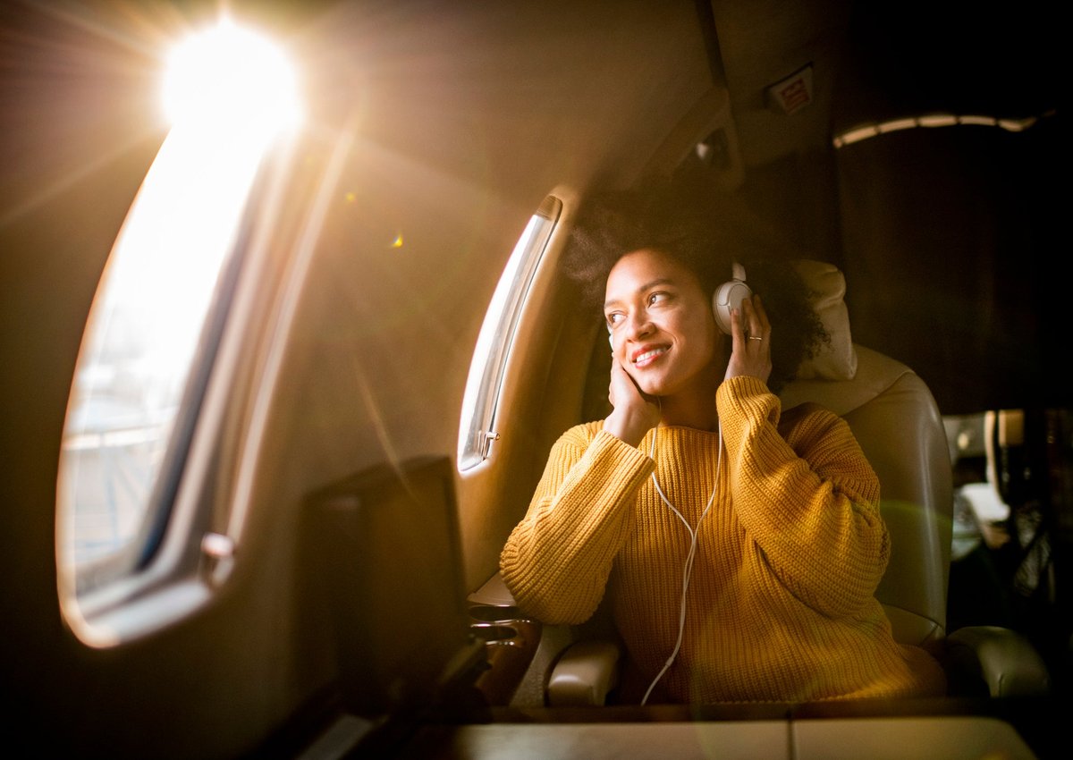A smiling airplane passenger listening to music and looking out the window.