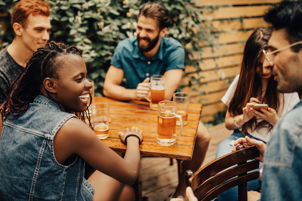 Group of friends drinking beer and laughing at a patio table in a restaurant.