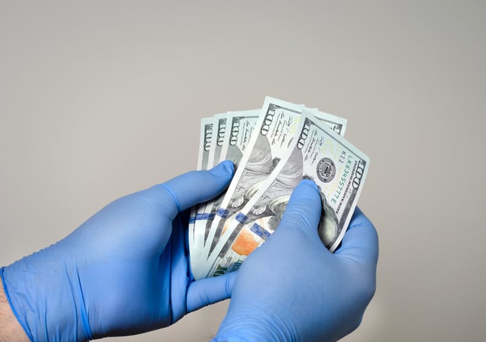 GLoved hands hold hundred-dollar bills.