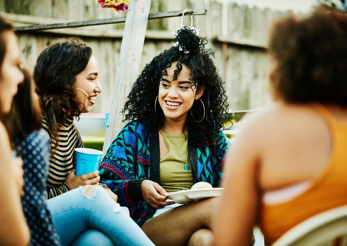 A group of friends sitting outside with plates and glasses in their hands.