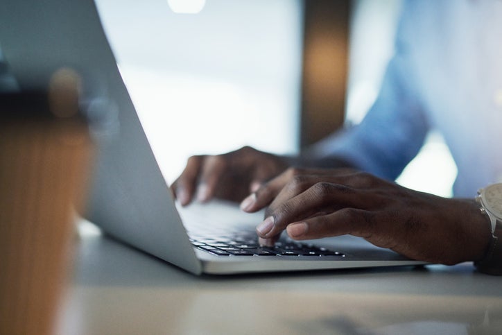 A man's hands typing on a laptop keyboard.