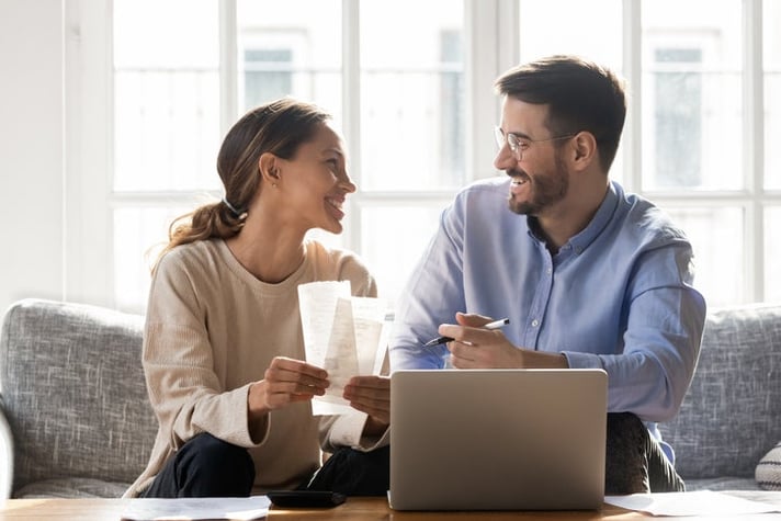 A happy couple on a couch with receipts and a laptop.