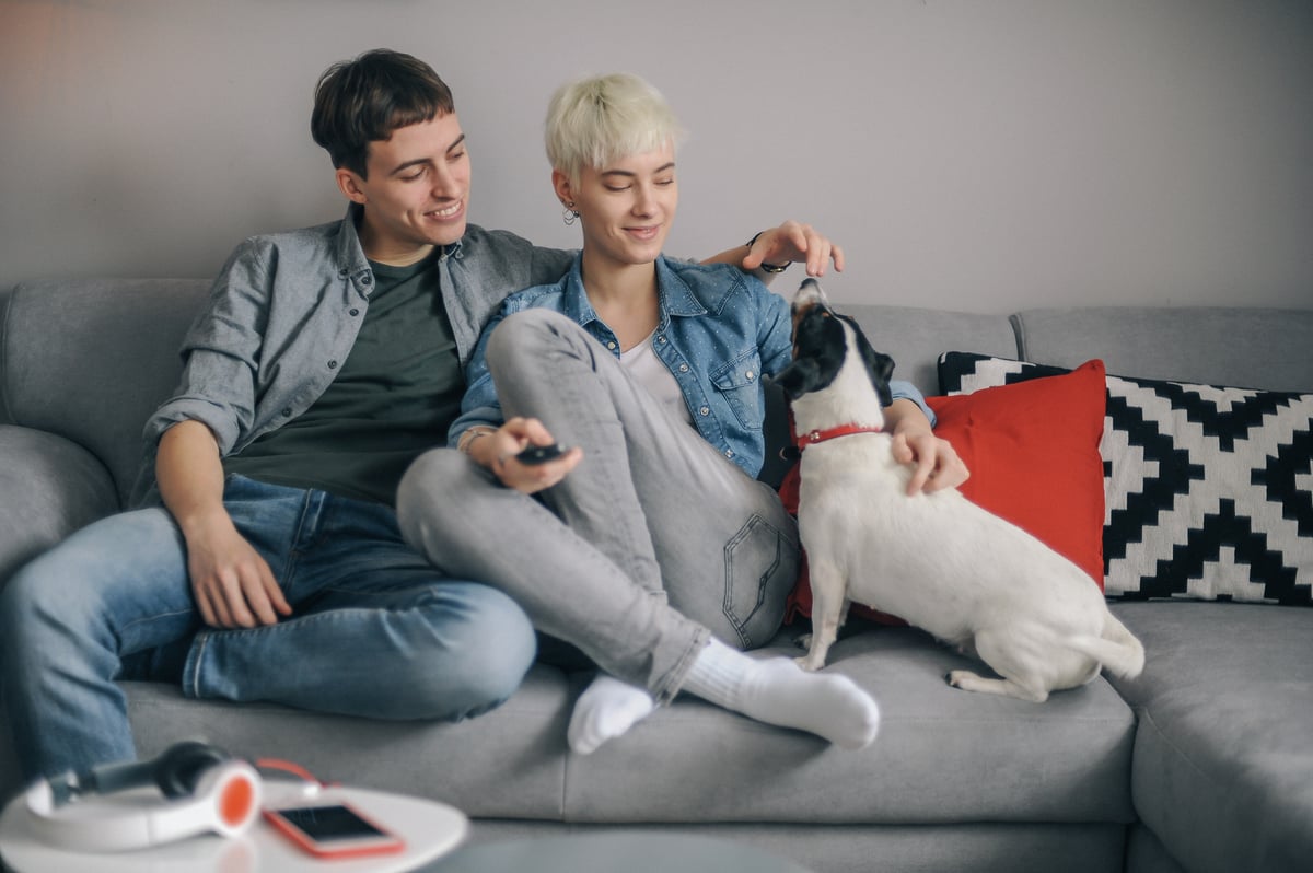 A happy young couple sitting on their couch with their dog.