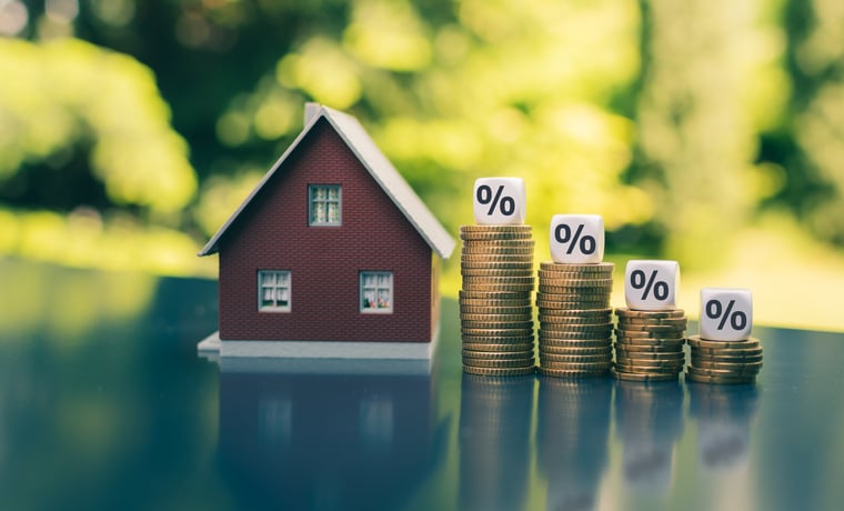 Stacks of coins with percent signs on top sit beside a small house