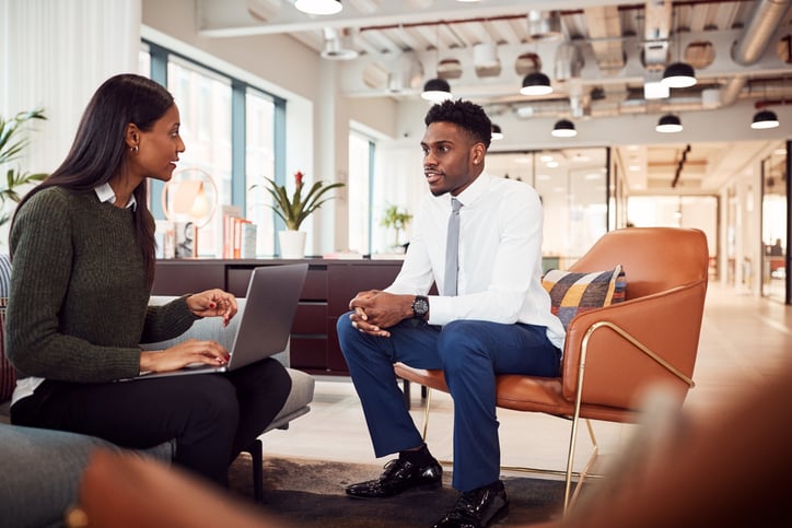 A woman asking a man questions in a job interview in a casual office setting.